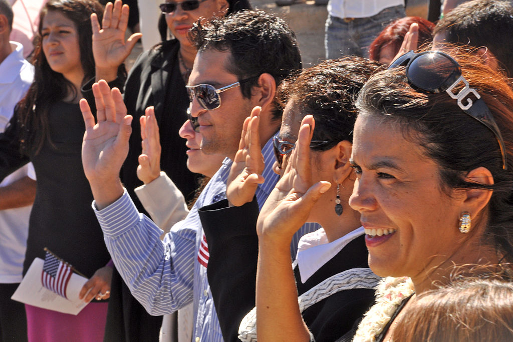 Women and men holding right hands up to swear an oath, small US flags visible