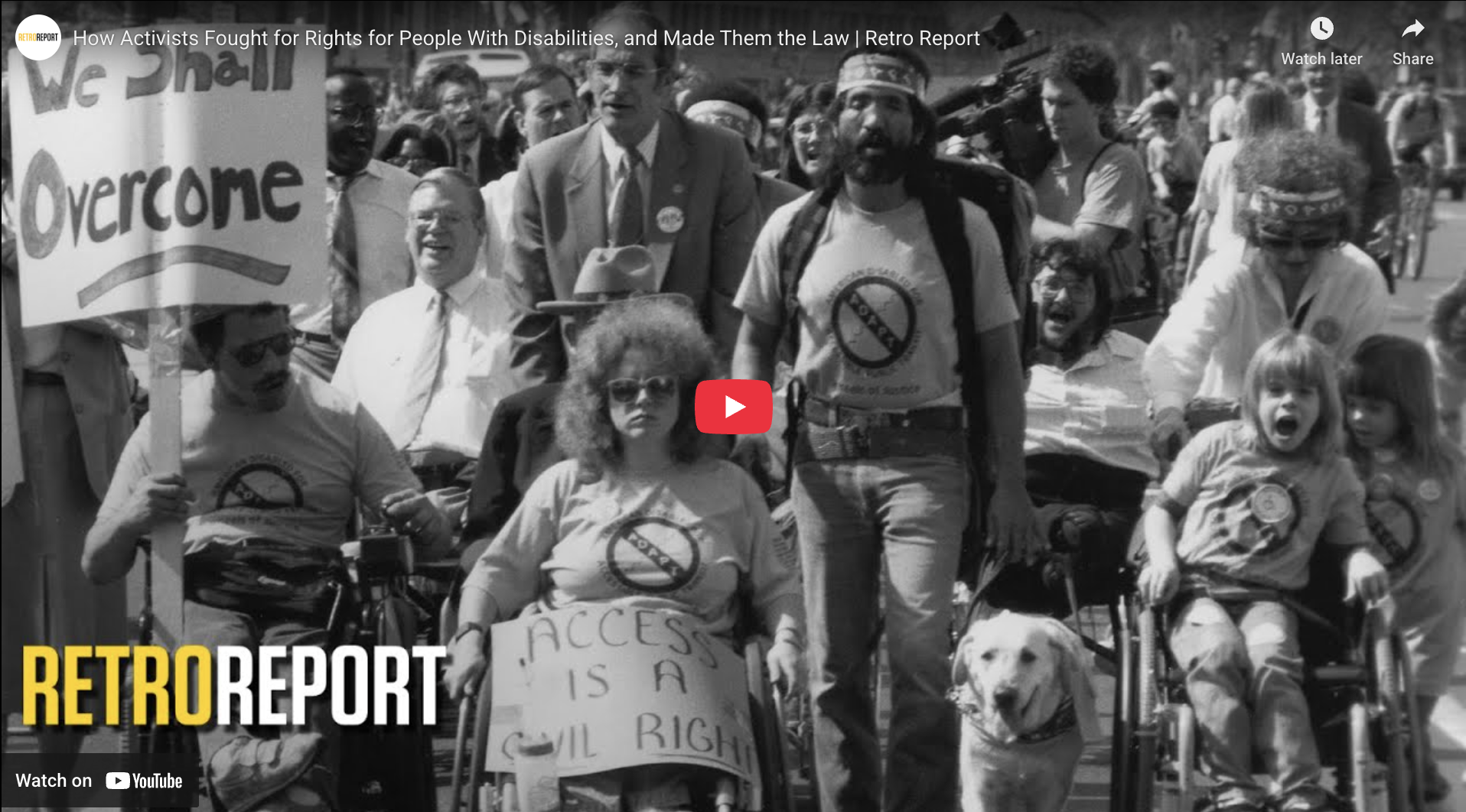 "Screenshot from RetroReport film on the Disability Rights Movement shows the front of a column of disability rights marchers, including one holding a banner that reads We Shall Overcome"