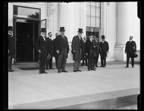 President Taft, Justice Oliver Wendall Holmes Jr., and several other men pose in front of the White House, wearing formal jackets and top hats. 