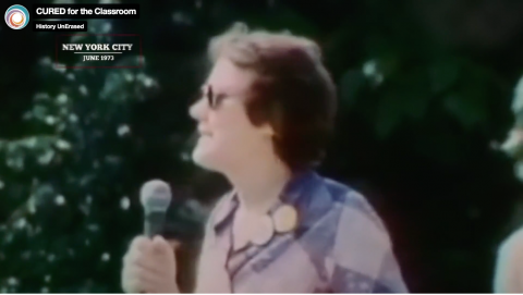 Screenshot from film Cured of a person in sunglasses speaking into a microphone