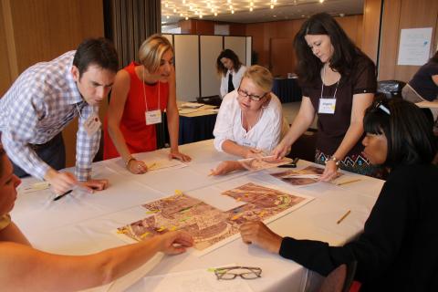 Five teachers, one man and four women all with name tags intently study large pieces of a map on a table at the Library of Congress
