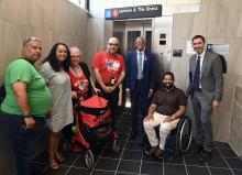 A diverse group of New Yorkers with a variety of disabilities and elected representatives pose by an MTA subway elevator.