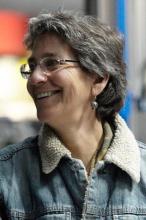 A woman with short grey hair is laughing and looking off camera. She wears a jeans jacket with fur lining.