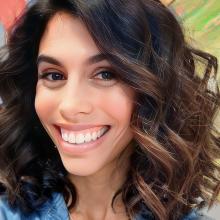 A white woman with shoulder length dark hair flashes a brilliant smile