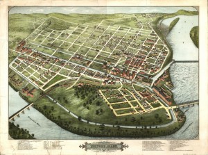 View from above of green land encircled by the Connecticut River, showing bridges, dam, and grid of streets and canals with brick factories and smaller houses.