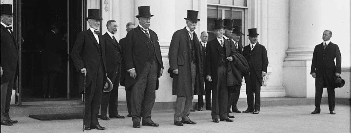 A photo of a group of older men wearing suits and top hats outside of the White House. Supreme Court Justice Oliver Wendell Holmes, Jr. stands in the center of the group, his trademark large white mustache is visible. 