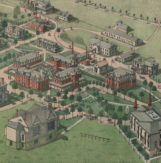 An aerial view shows dozens of large and small wood and brick buildings on a campus with many trees and surrounded by grassy fields.