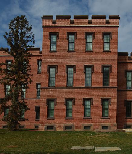 A brick building of two stories with multiple wings and towers of three stories. 