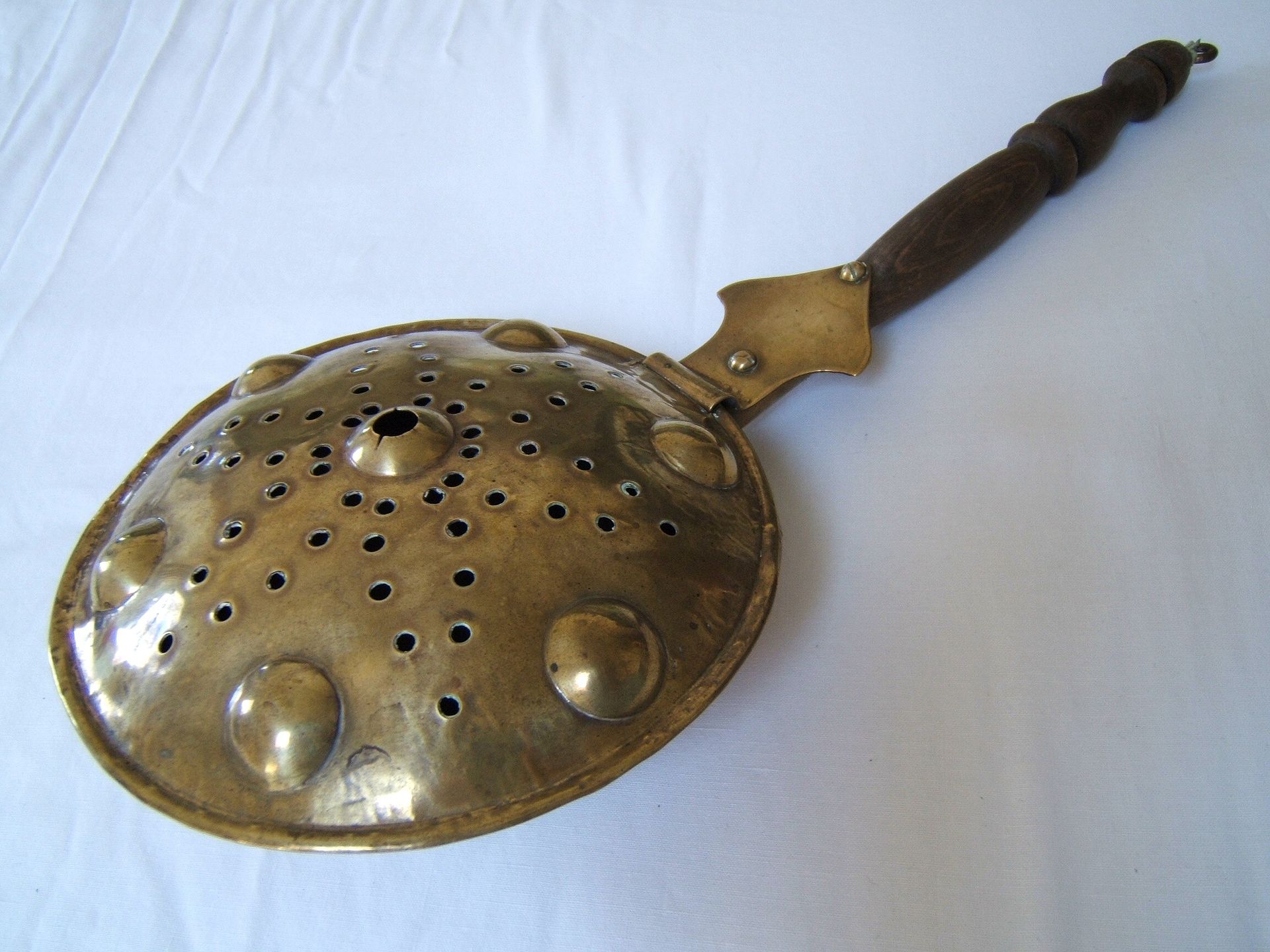 a round metal pan with a curved lid with many round holes and wooden handle