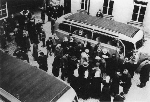 1941 photo from above shows dozens of people in jackets and hats  standing in a cobbled courtyard near a bus parked with the door open