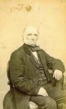 Posed photo of seated man in coat and vest.