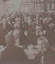 Hundreds of veterans sit at tables in a huge dining hall with high rafters.