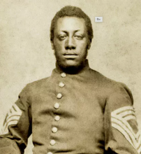 A young Black Union soldier sits with his hands on his thighs. His uniform has the three chevron patches of a sergeant-major. This Carte de Visite bears the name Sergt. Major Lewis Douglass. Case & Getchell. Boston. 