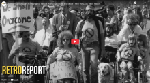 "Screenshot from RetroReport film on the Disability Rights Movement shows the front of a column of disability rights marchers, including one holding a banner that reads We Shall Overcome"